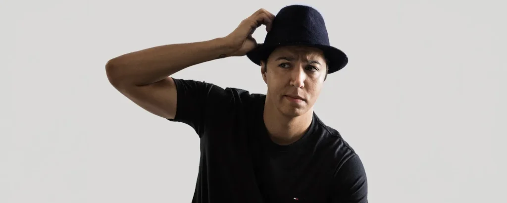 A young male wearing a black hat and black t-shirt scratching his head