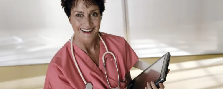 A smiling nurse wearing pink scrubs with a stethoscope around her neck.